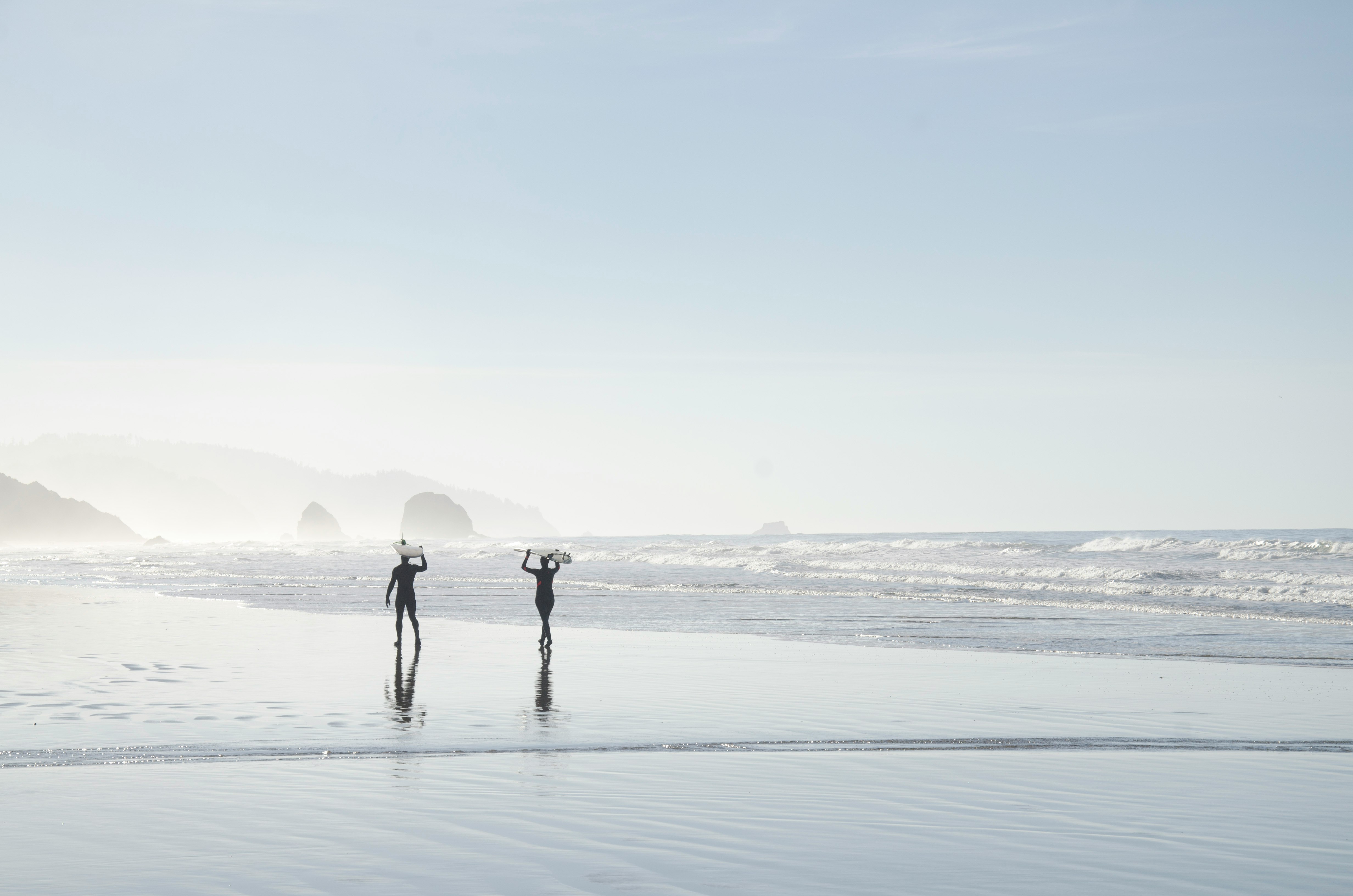 two men carrying surfboards near body of water